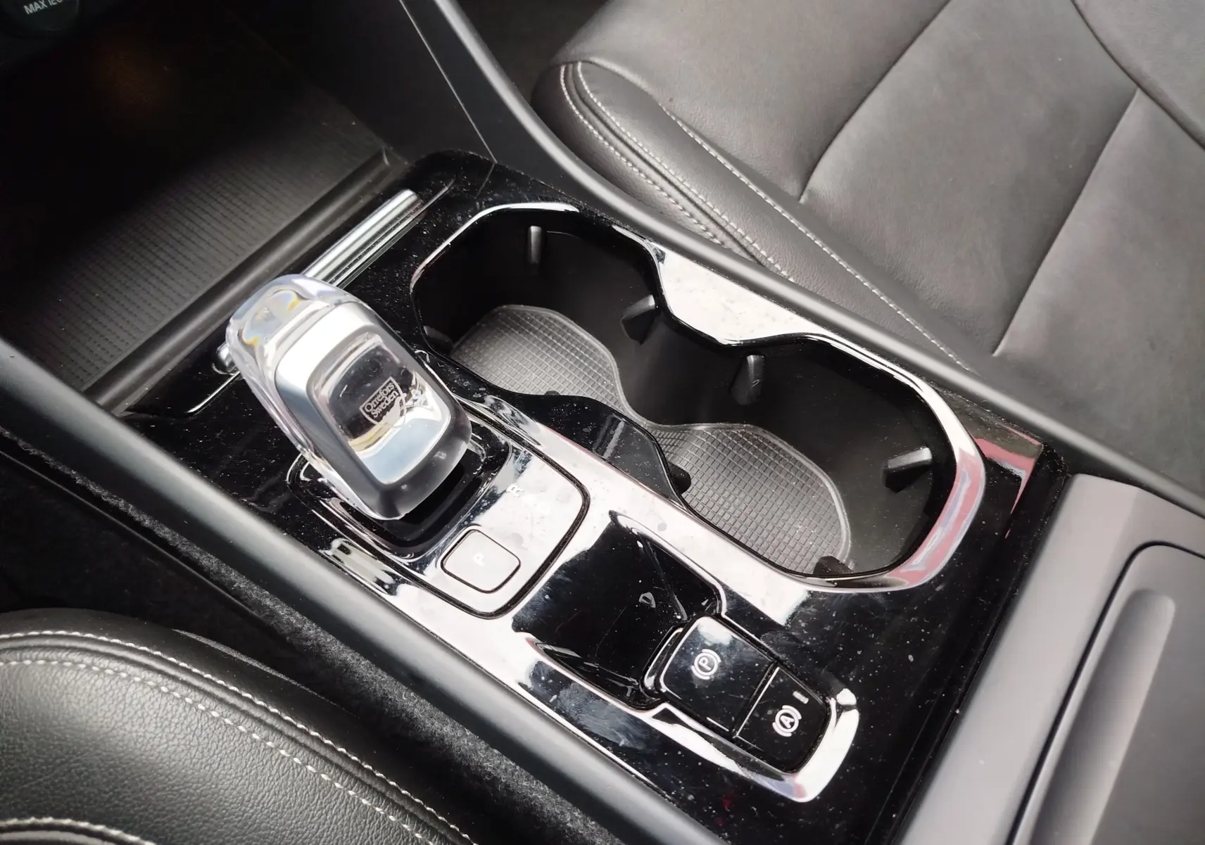 Gros plan sur la console centrale noire avec levier de vitesse cristal et porte-gobelets, siège en cuir noir visible, Volvo XC40.