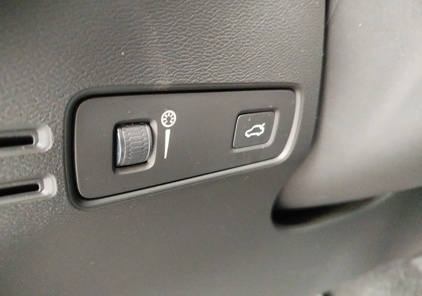 Gros plan sur les commandes intérieures noires du tableau de bord du Volvo XC40 beige, bouton d'ouverture de coffre visible.