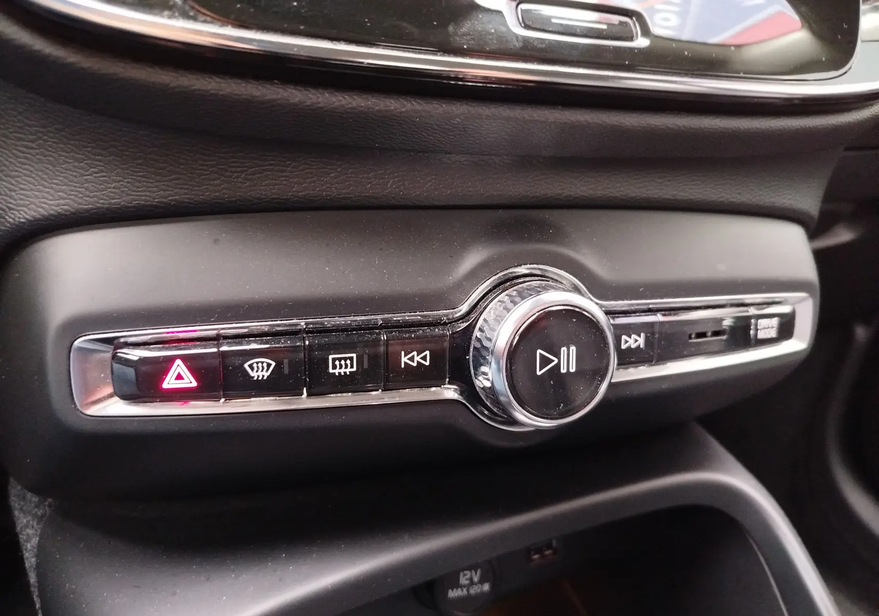 Gros plan sur la console centrale noire du Volvo XC40 beige, avec boutons de commande média et signal d’alerte allumé.