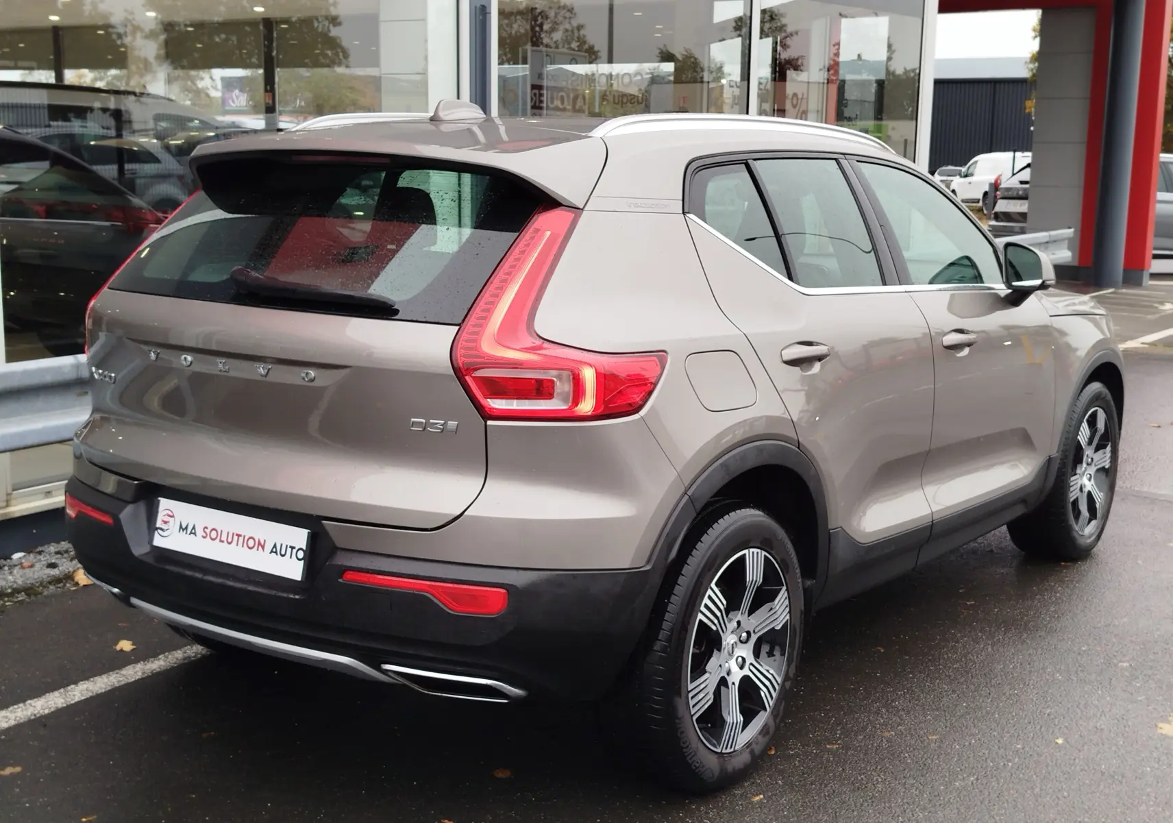 Vue 3/4 arrière droite d'un Volvo XC40 beige 2020 avec feux arrière en forme de C et jantes bi-ton.