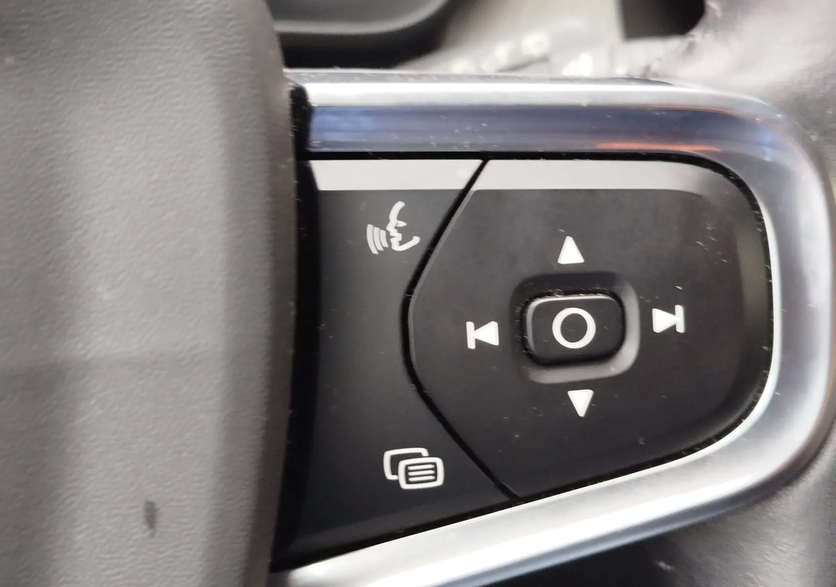 Gros plan sur les commandes noires du volant côté gauche du Volvo XC40 beige, avec boutons de navigation et téléphone.