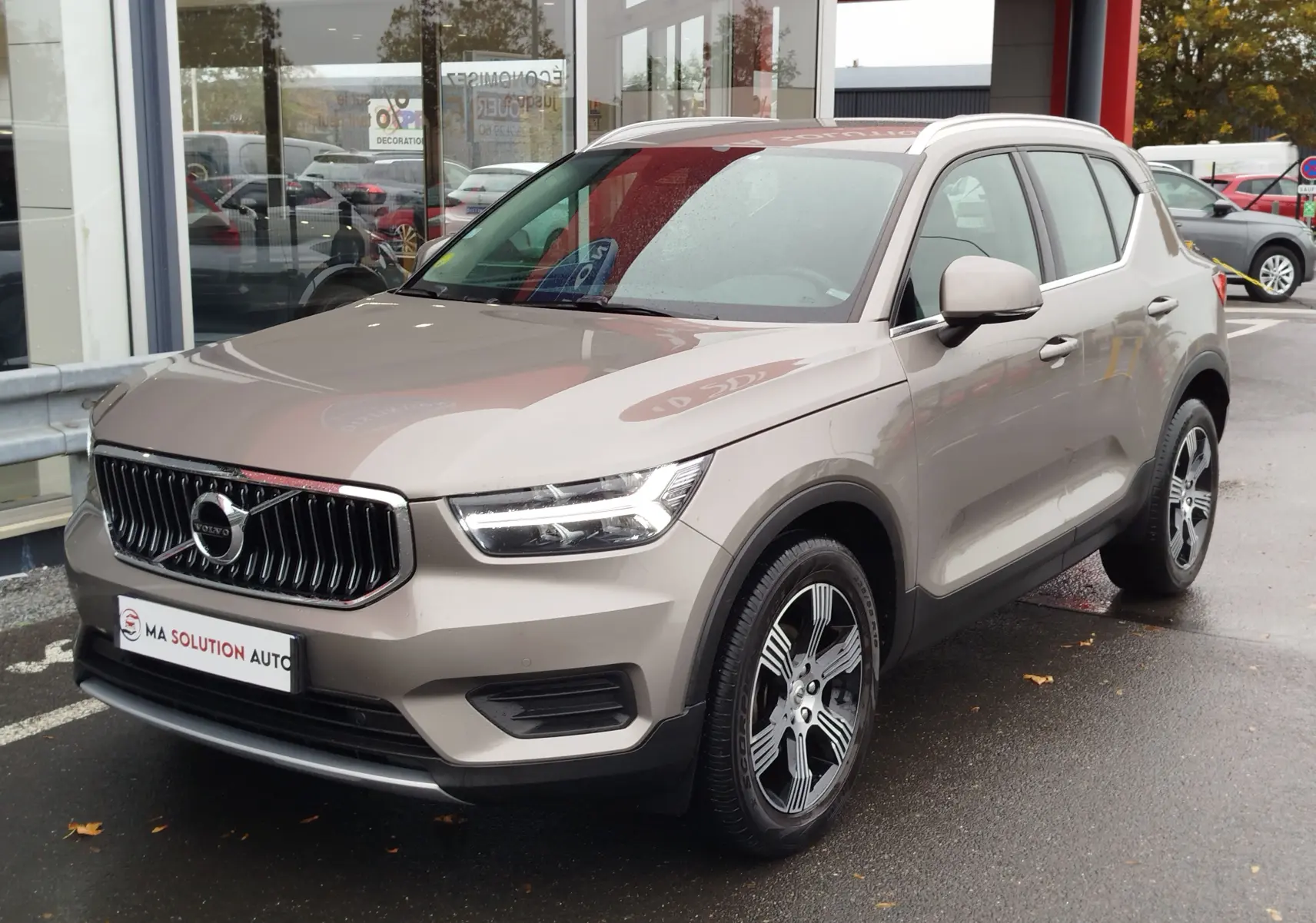 Volvo XC40 beige vue 3/4 avant droit, avec calandre verticale chromée et jantes alliage bicolores.