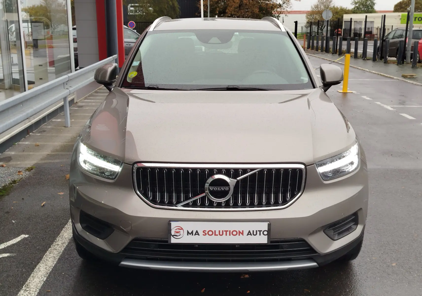Vue frontale d'un Volvo XC40 beige 2020 avec phares allumés, calandre chromée et plaque "Ma Solution Auto".