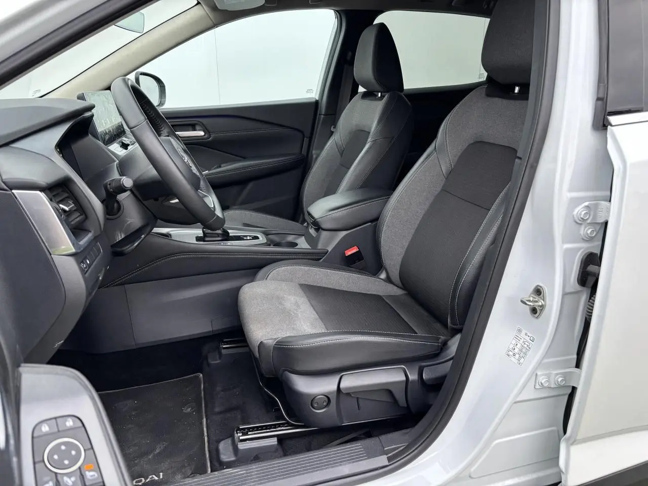 Vue intérieure côté gauche du Nissan Qashqai blanc nacré 2025, montrant les sièges avant en tissu noir et gris.
