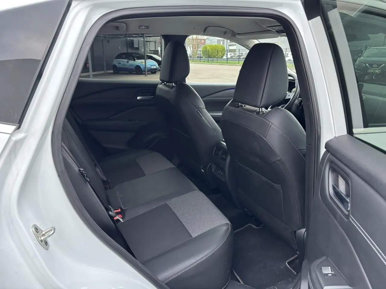 Vue intérieure côté gauche de la banquette arrière noire et grise du Nissan Qashqai blanc nacré 2025, portes ouvertes.