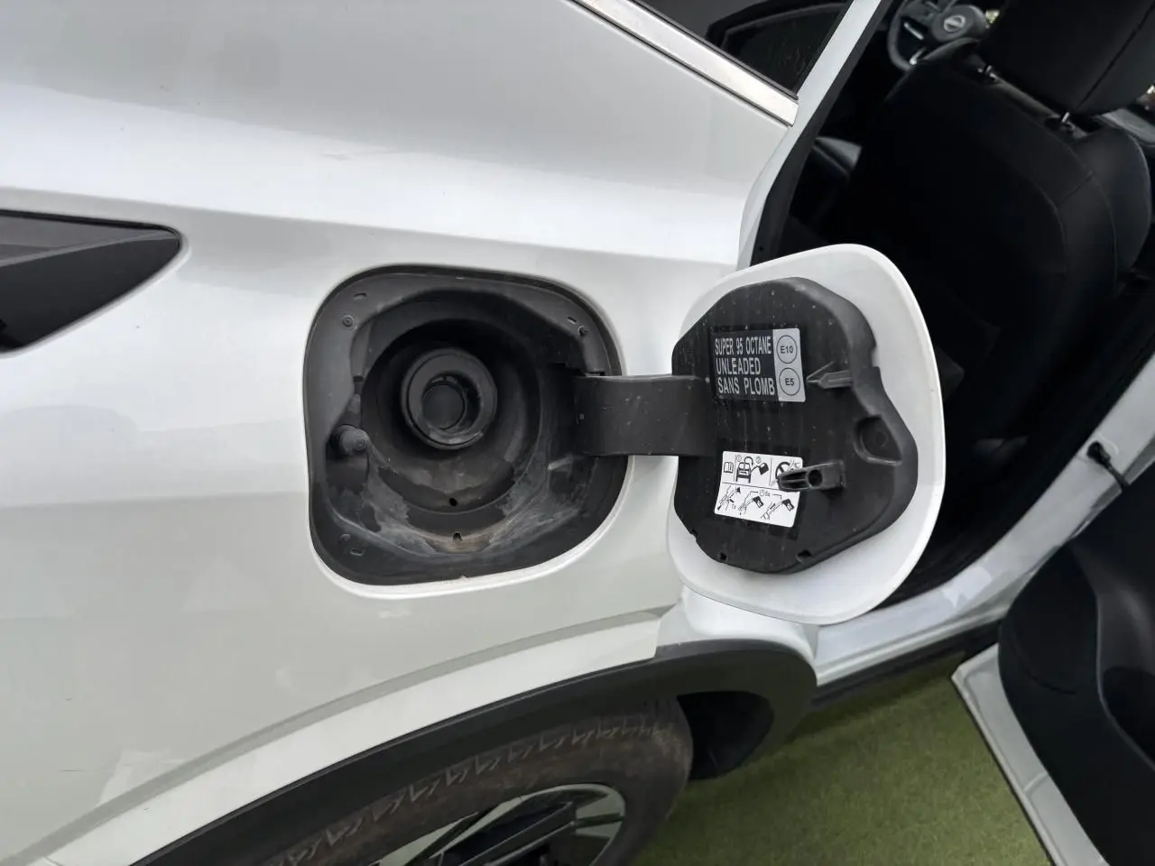 Vue rapprochée de la trappe à carburant ouverte côté gauche d’un Nissan Qashqai blanc nacré avec porte arrière ouverte.