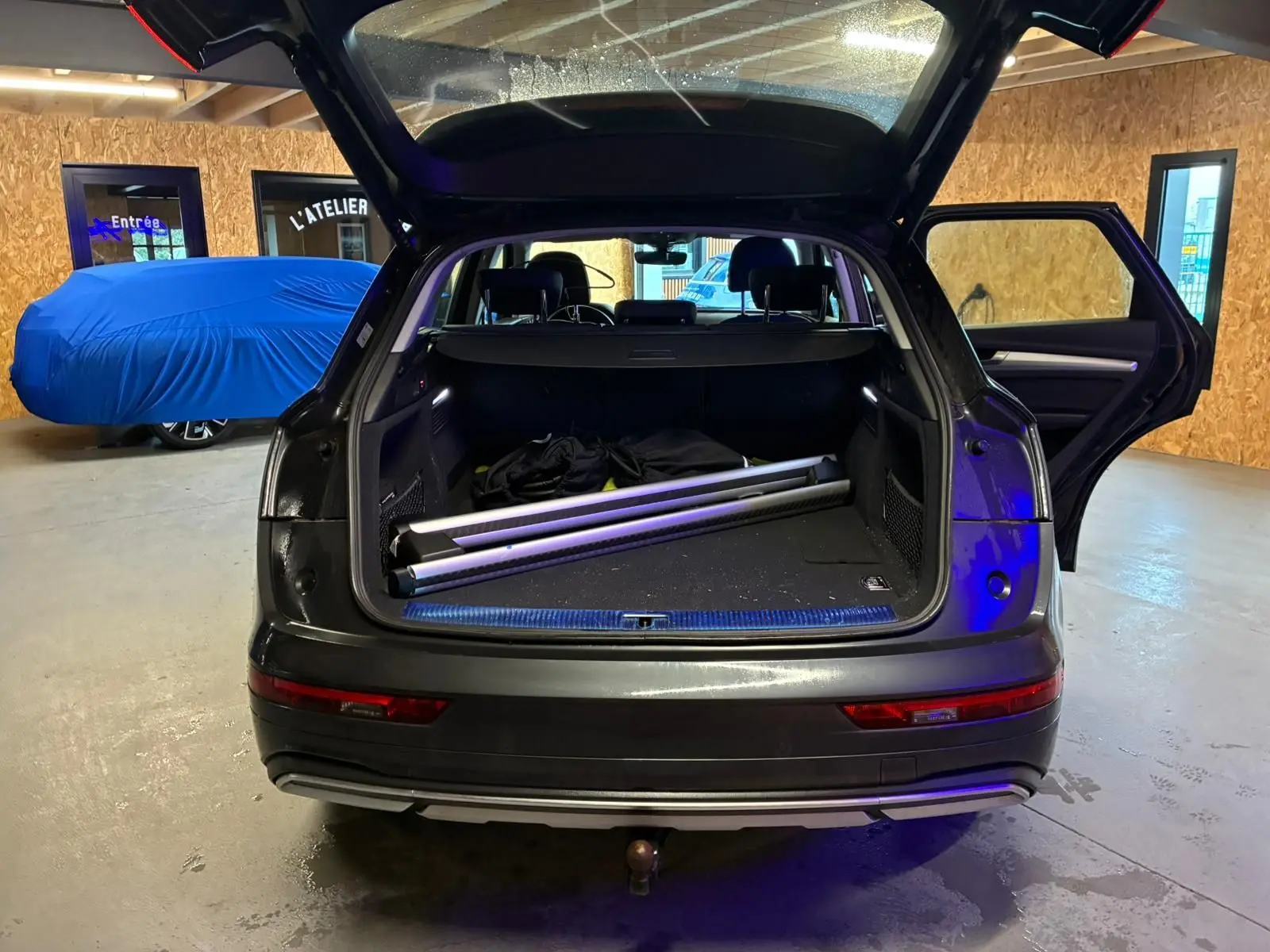 Vue arrière d'un Audi Q5 gris 2024 avec coffre ouvert et porte arrière droite ouverte, montrant un crochet d'attelage.