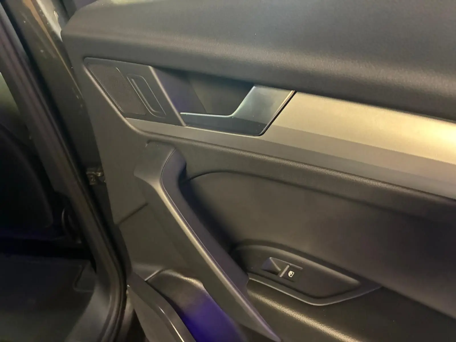 Gros plan sur la porte intérieure côté gauche de l'Audi Q5 gris, avec poignée et commande de vitre intégrée.