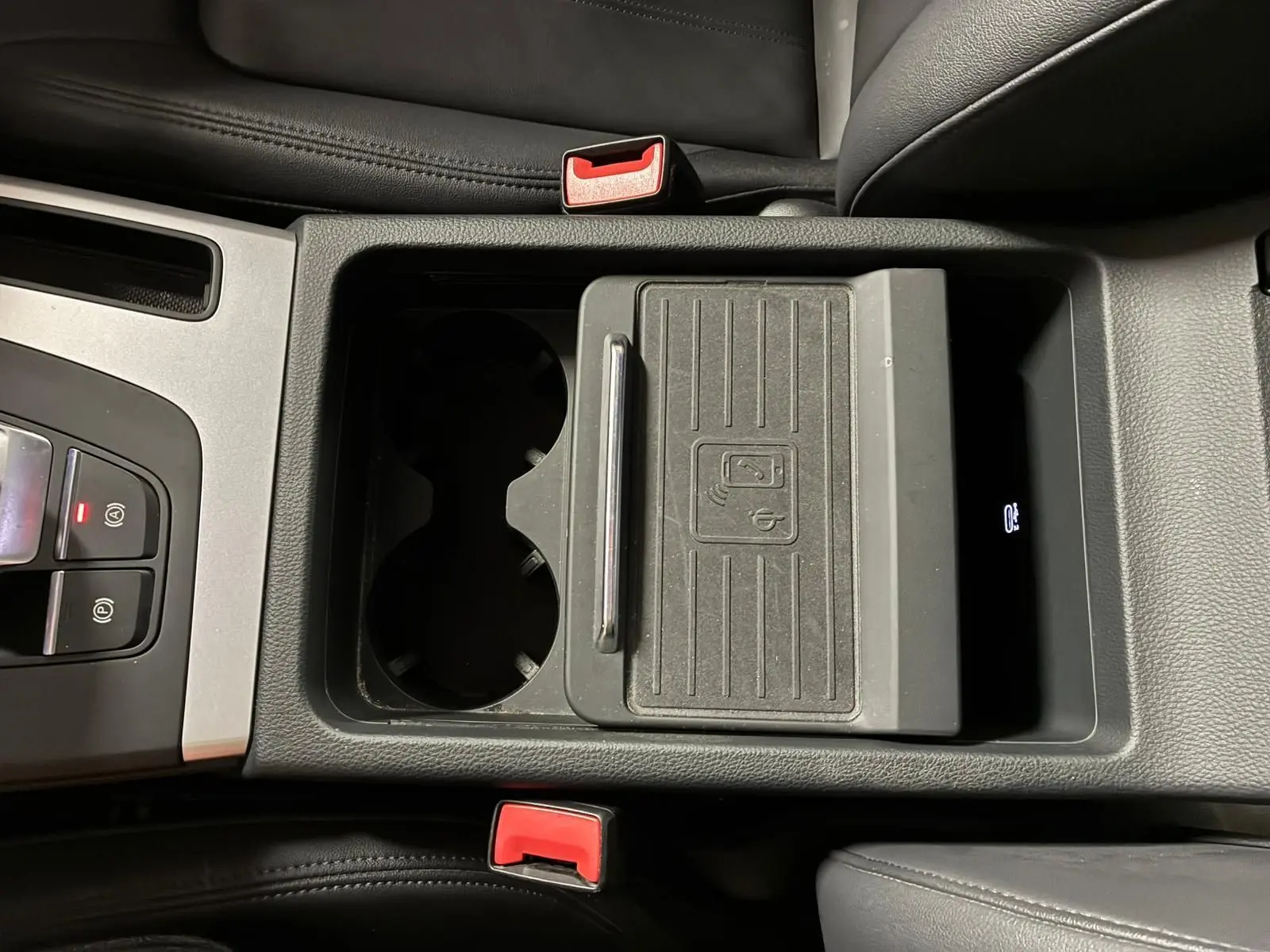 Vue plongeante sur la console centrale noire de l'Audi Q5 2024 avec porte-gobelets et chargeur sans fil.