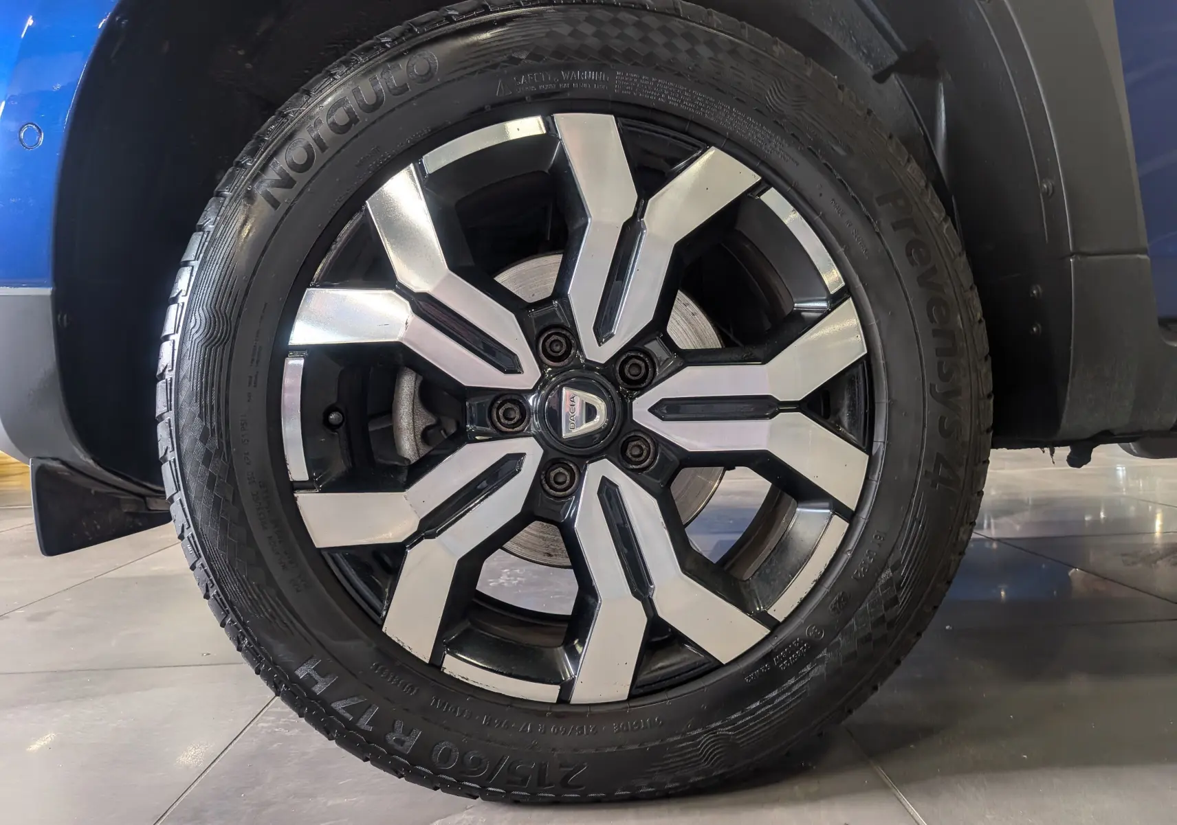 Gros plan sur la roue avant gauche du Dacia Duster 2022 Bleu Iron, avec jante alliage bicolore distinctive.