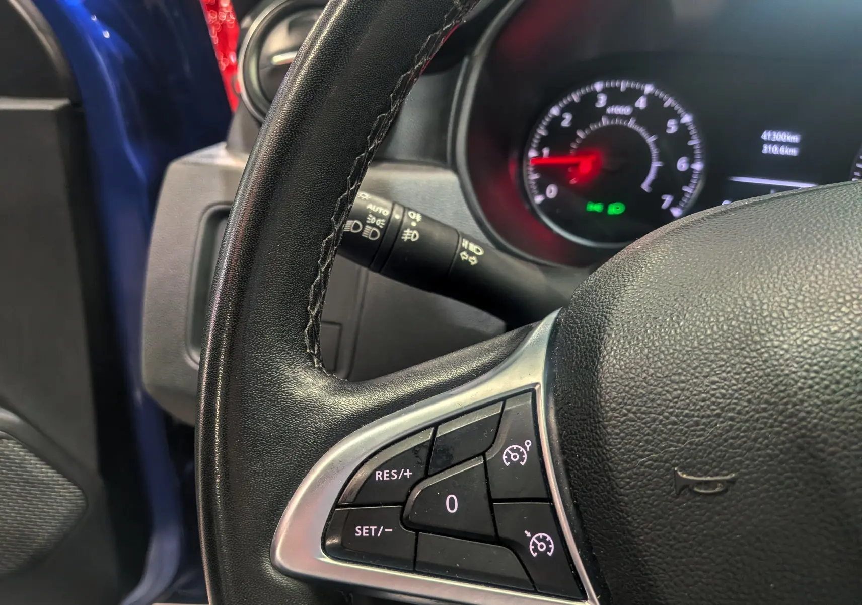 Gros plan sur le volant côté gauche du Dacia Duster bleu Iron, avec commandes de régulateur de vitesse et tableau de bord en arrière-plan.