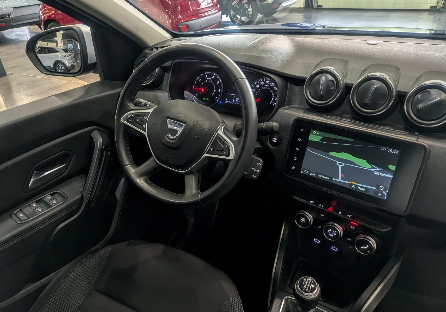 Vue intérieure côté conducteur du Dacia Duster 2022, tableau de bord noir avec écran tactile et volant multifonction.