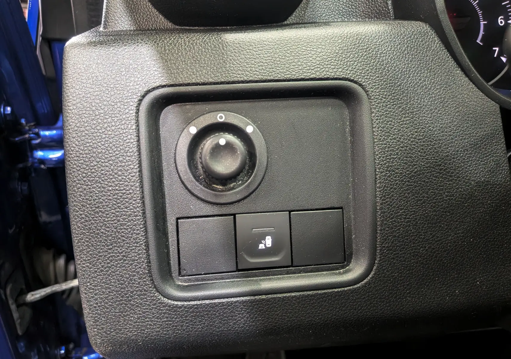Gros plan sur le panneau de réglage des rétroviseurs et verrouillage des portes du Dacia Duster bleu Iron côté conducteur.