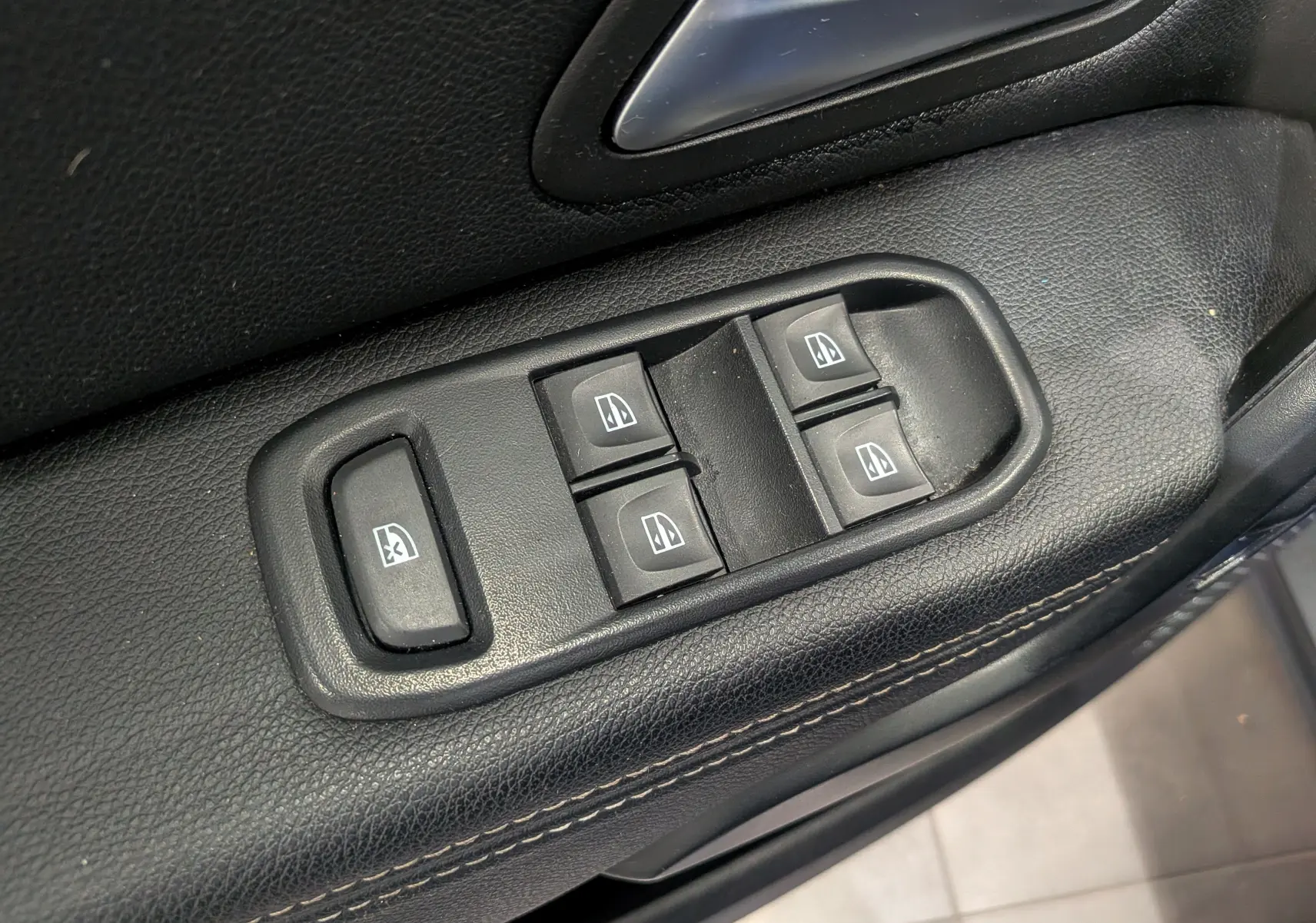 Gros plan sur les commandes électriques des vitres sur la portière côté conducteur du Dacia Duster 2022, intérieur noir.