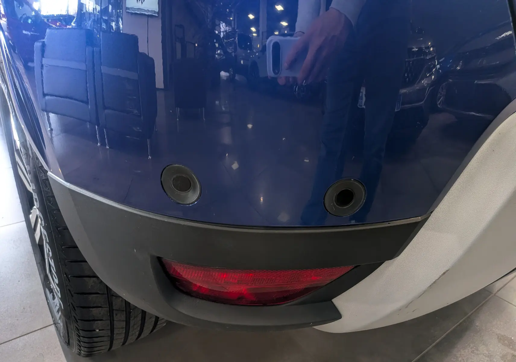 Gros plan sur le pare-chocs arrière bleu Iron du Dacia Duster 2022 avec capteurs de recul et feu antibrouillard rouge.