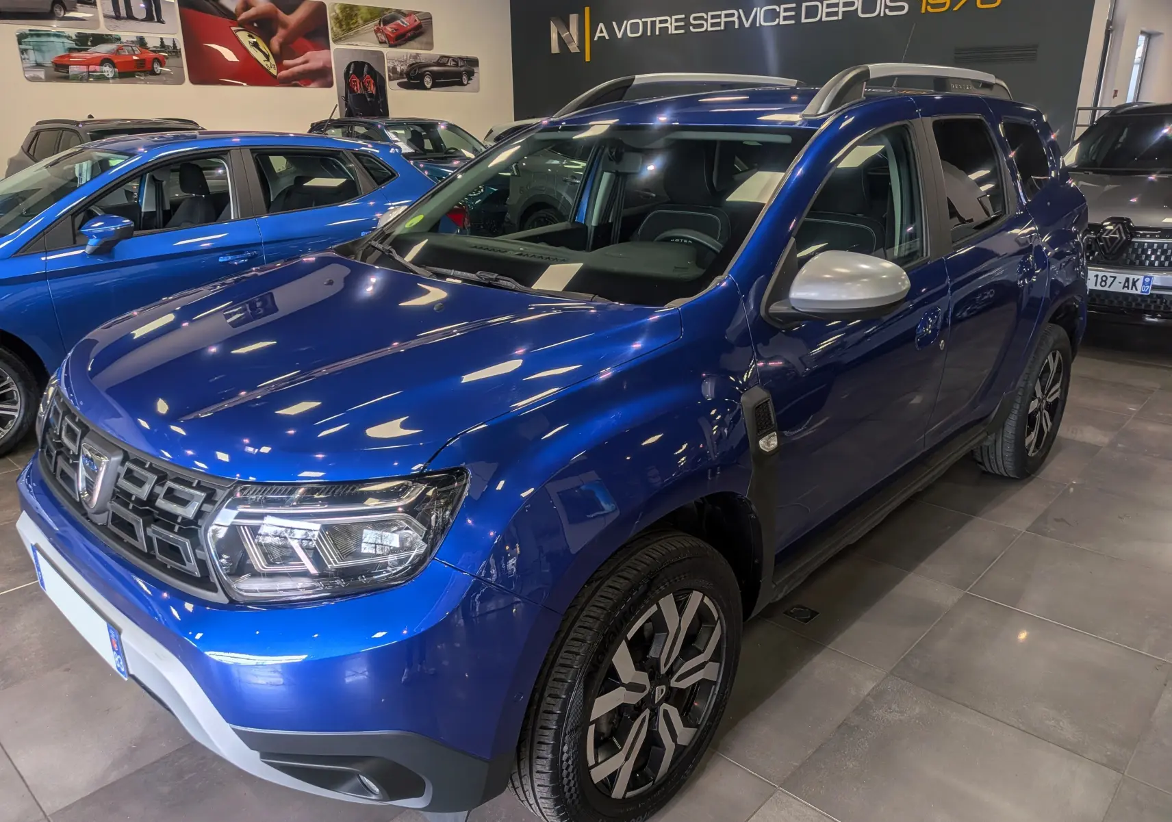 Vue 3/4 avant droite du Dacia Duster 2022 bleu Iron avec rétroviseurs argentés et jantes bi-ton en concession.