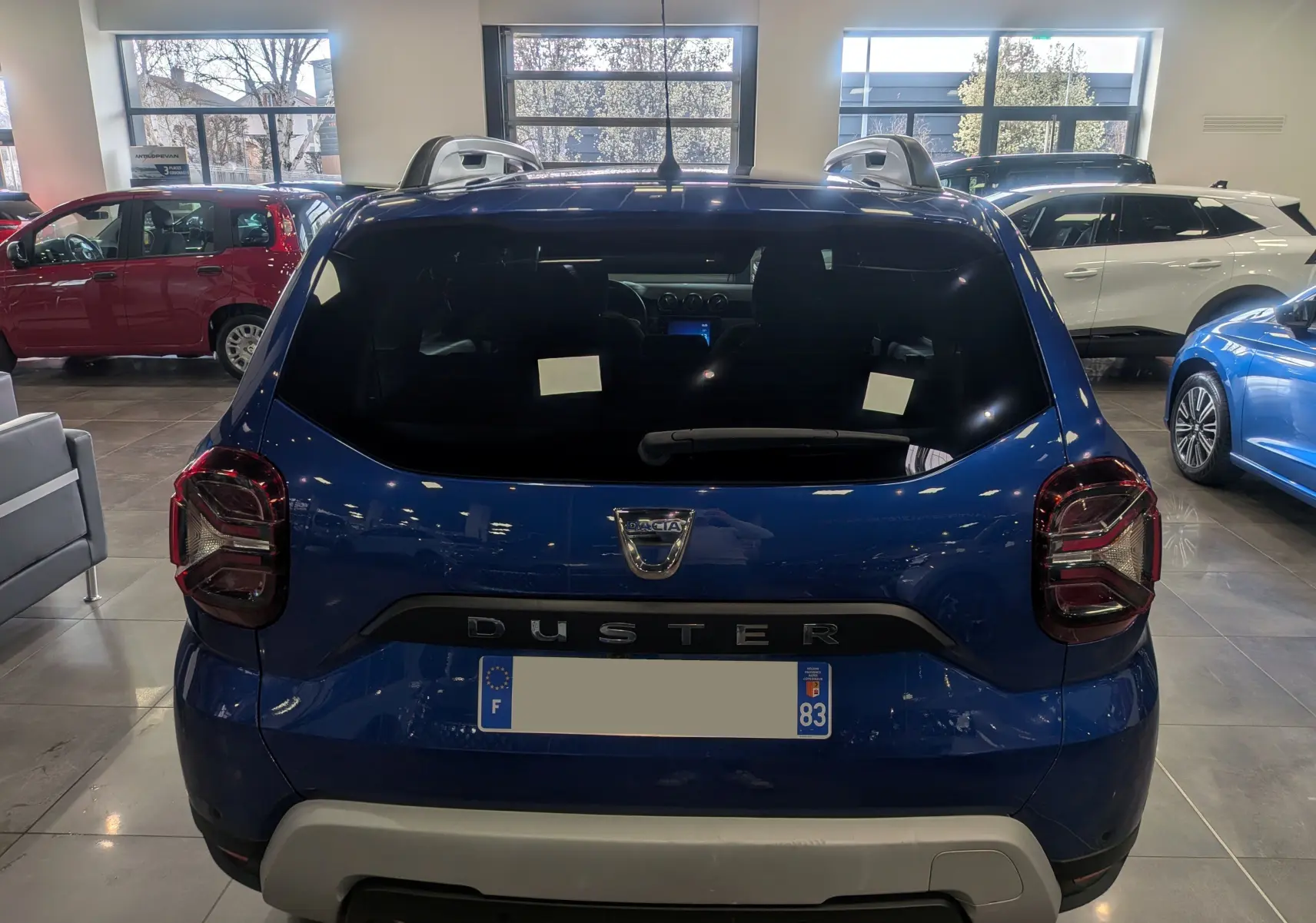 Vue arrière d'un Dacia Duster bleu Iron 2022 en showroom, avec logo et nom du modèle bien visibles.