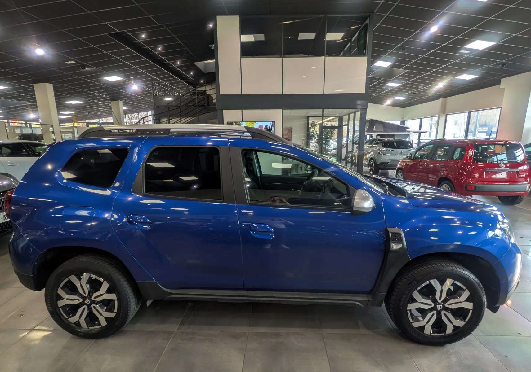 Vue de profil côté gauche d'un Dacia Duster 2022 bleu Iron avec jantes alliage bicolores en showroom.