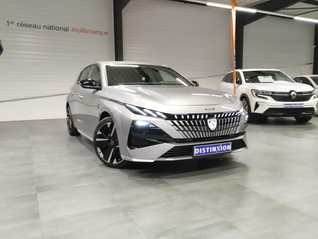 Vue 3/4 avant d'une Peugeot 308 gris Artense avec calandre lumineuse et jantes alliage noires en showroom.