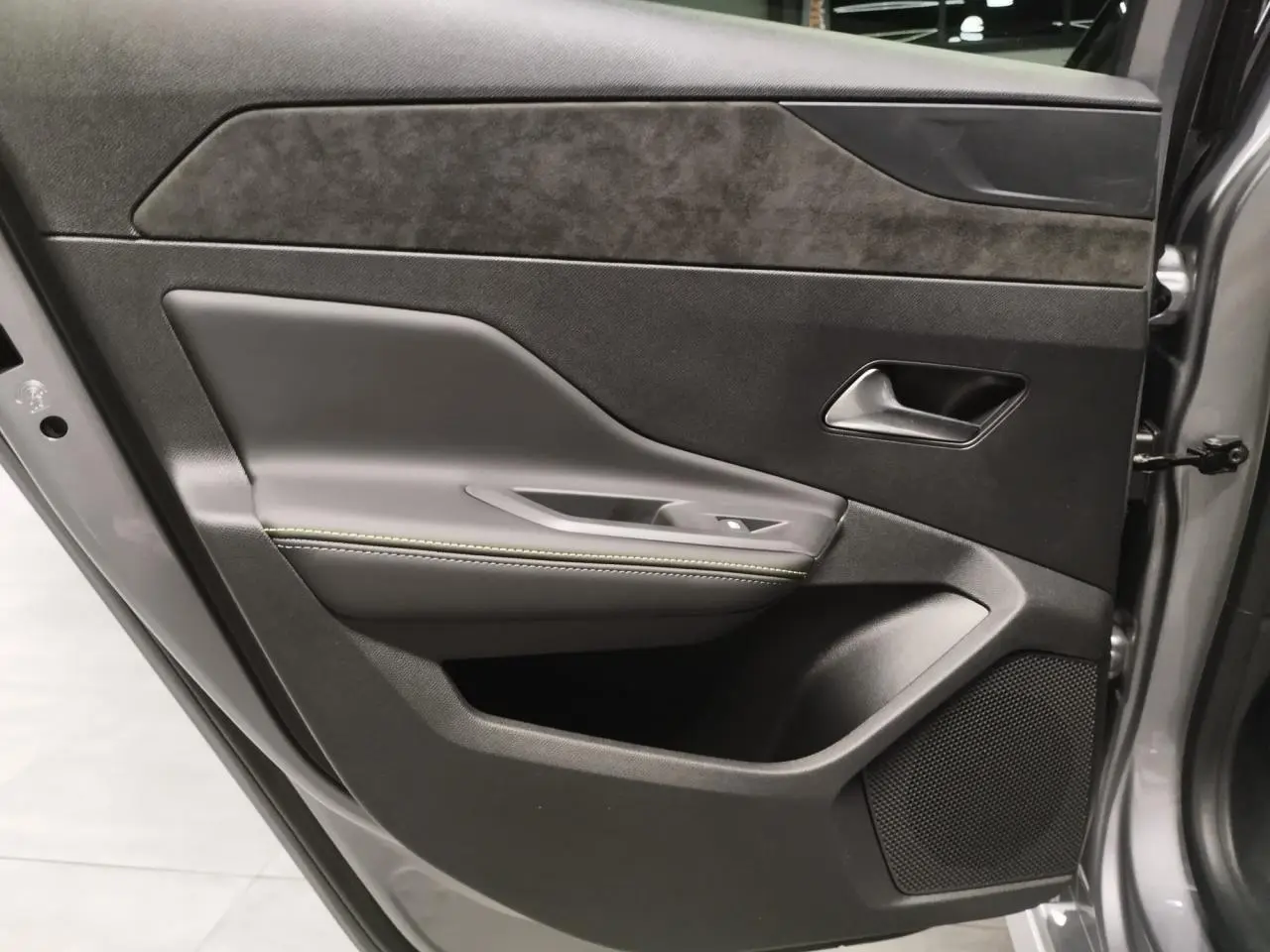 Gros plan sur la porte avant gauche gris Artense de la Peugeot 308 Hybrid avec surpiqûres vert Adamite et haut-parleur intégré.