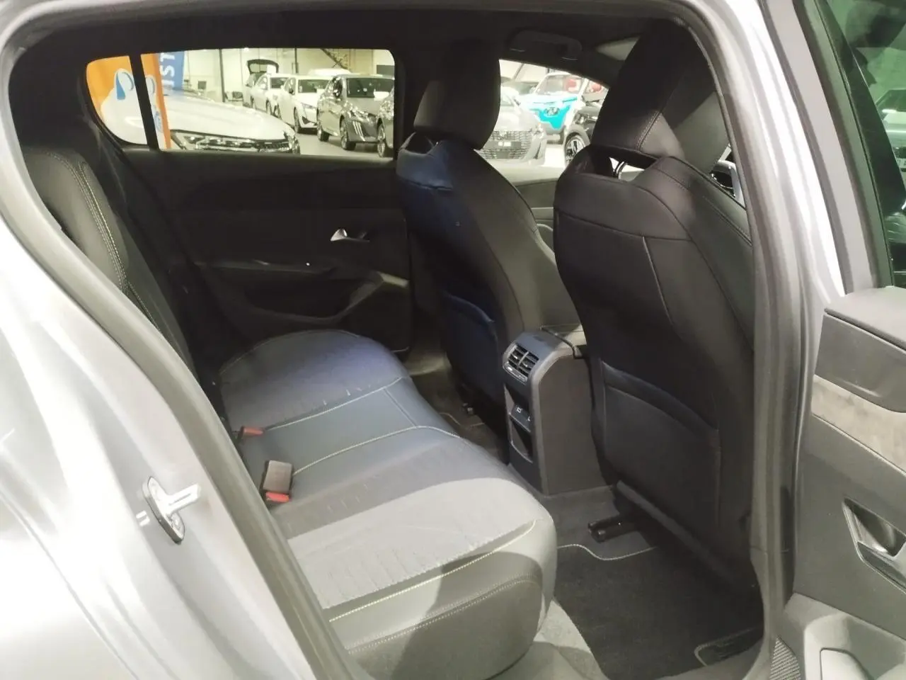 Vue intérieure arrière côté gauche d'une Peugeot 308 gris Artense, montrant la banquette et les sièges avant en tissu noir avec surpiqûres.