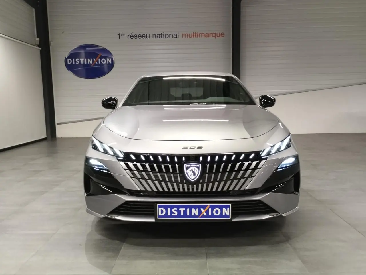 Vue avant d'une Peugeot 308 gris Artense avec calandre illuminée et phares LED allumés en intérieur showroom.