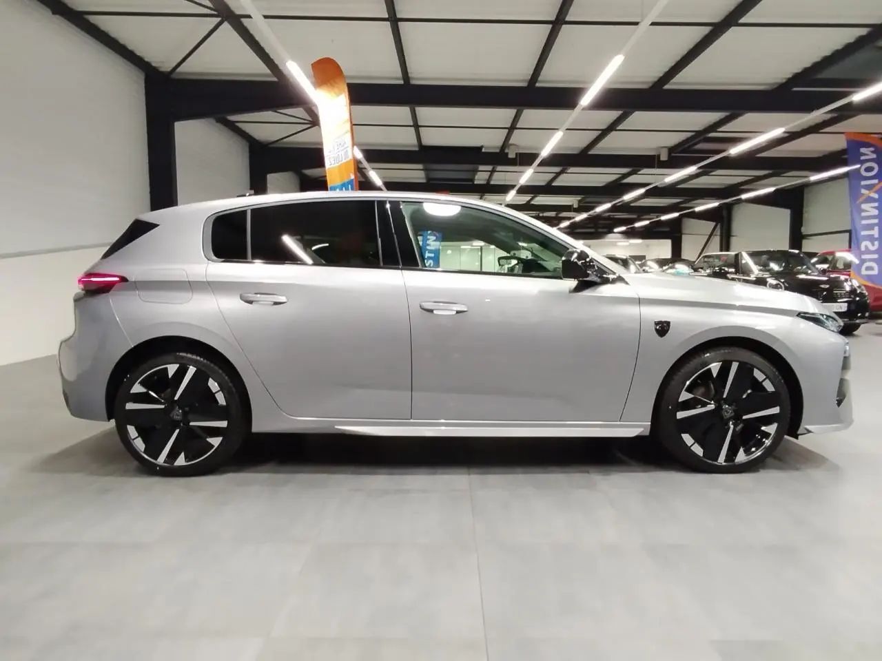 Profil droit d'une Peugeot 308 gris Artense avec jantes alliage noires et toit noir en intérieur d'exposition.