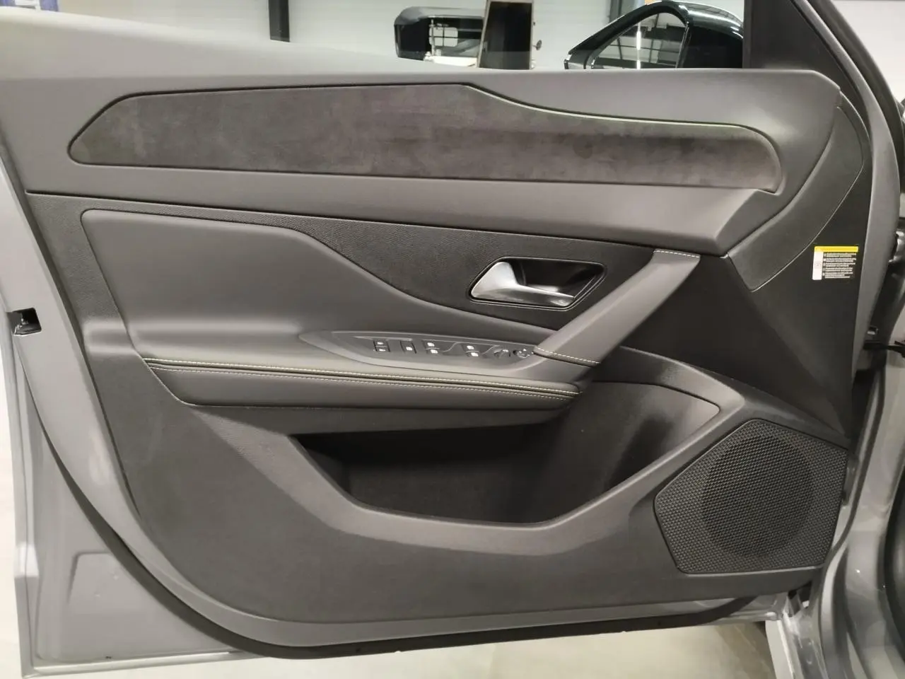 Vue rapprochée de la porte avant gauche gris Artense de la Peugeot 308 Hybrid avec surpiqûres vert Adamite et haut-parleur intégré.