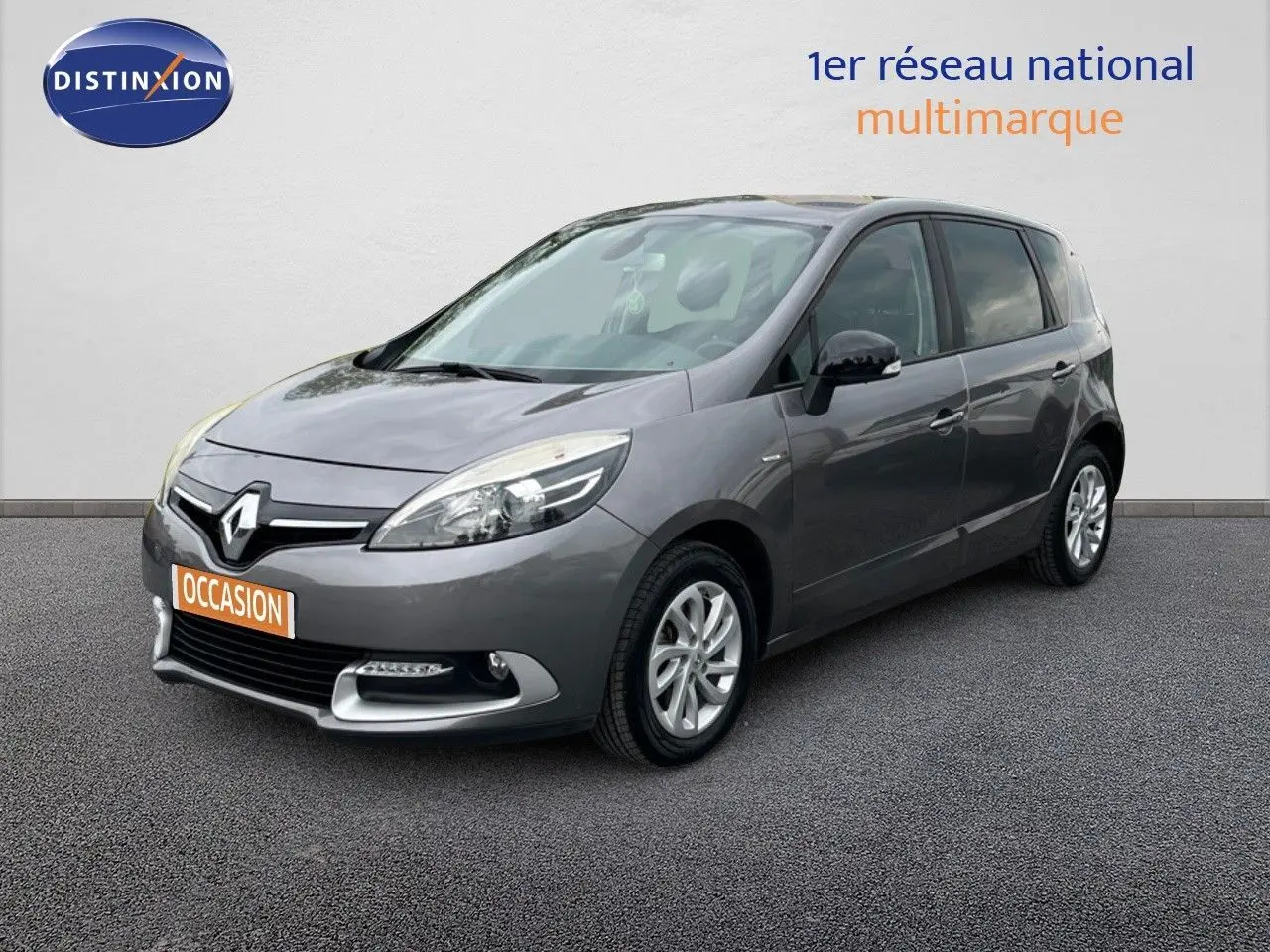 Renault Scénic III gris en 3/4 avant droit, avec calandre chromée et feux avant profilés visibles.