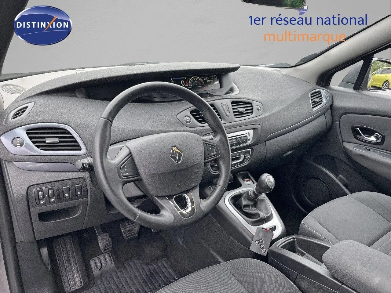Vue intérieure côté conducteur du Renault Scénic III gris de 2015, montrant le volant, tableau de bord et levier de vitesse manuel.