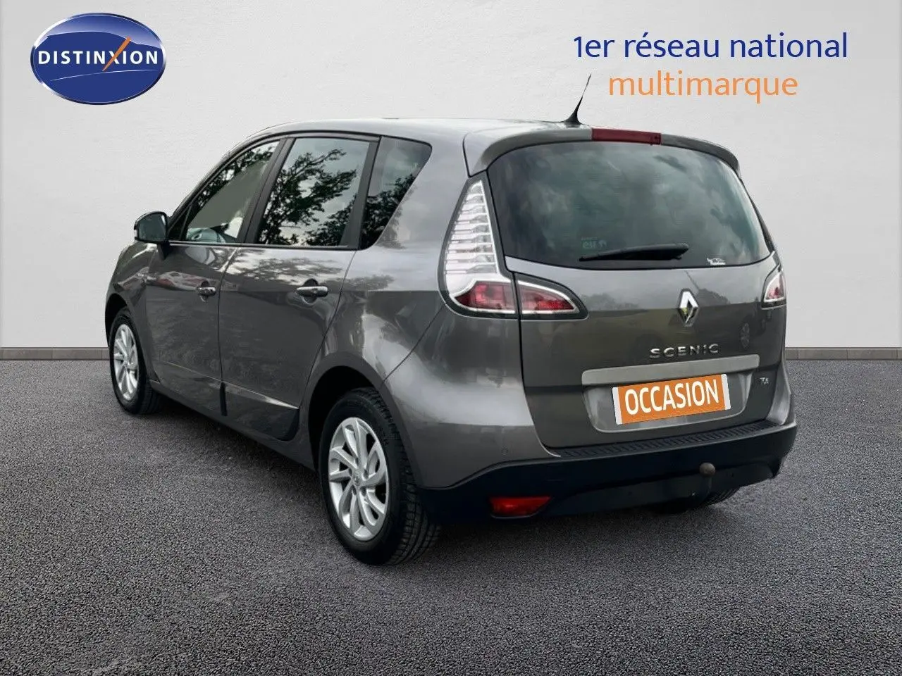 Renault Scénic III gris en 3/4 arrière gauche, avec logo et plaque "OCCASION" visible sur un fond neutre.