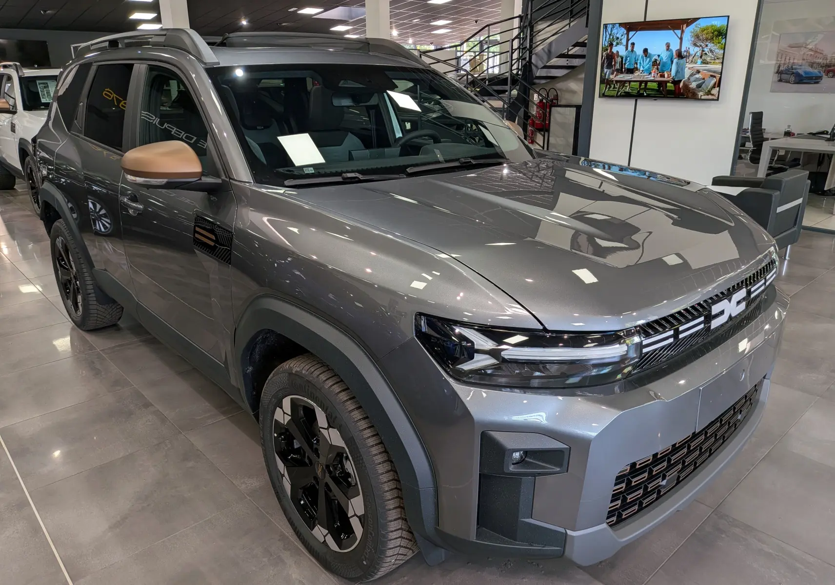 Vue 3/4 avant droite du Dacia Bigster Hybrid-G 150 4x4 Extrême gris schiste avec rétroviseurs bronze en showroom.