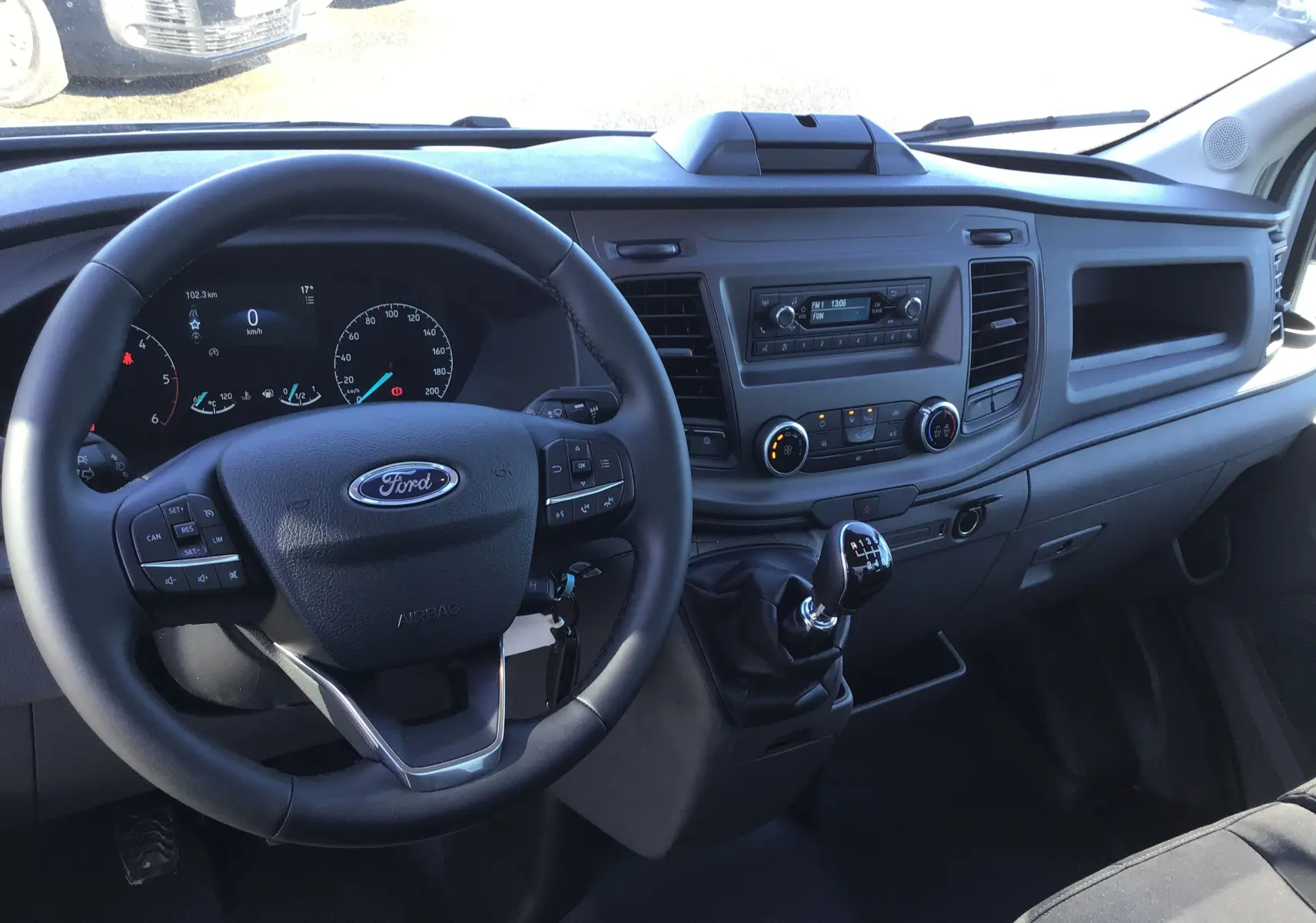 Vue intérieure du tableau de bord et volant du Ford Transit Chassis Cabine blanc, avec levier de vitesses manuel visible.