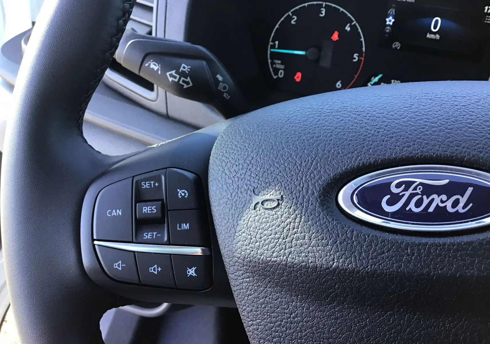 Gros plan sur le volant noir du Ford Transit Chassis Cabine blanc, avec commandes de régulateur de vitesse visibles.
