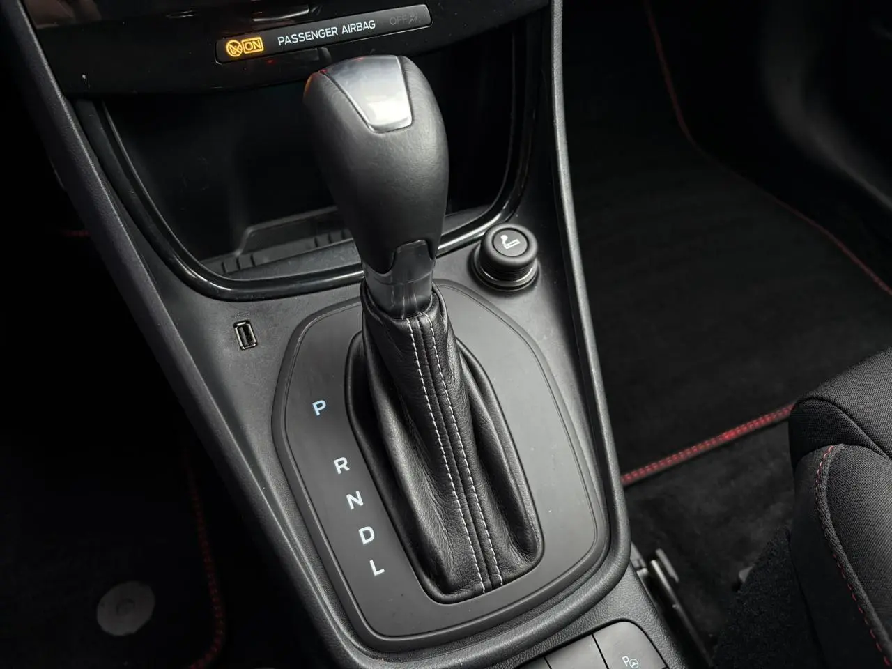 Gros plan sur la console centrale du Ford Puma 2023, levier de vitesses automatique en cuir noir avec surpiqûres rouges.