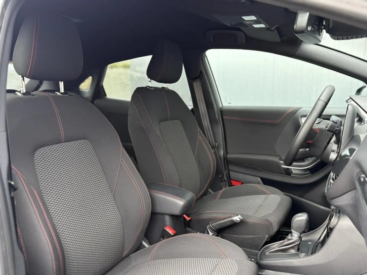 Vue intérieure côté droit du Ford Puma gris Solar 2023, sièges tissu noir avec surpiqûres rouges et volant ST-Line.