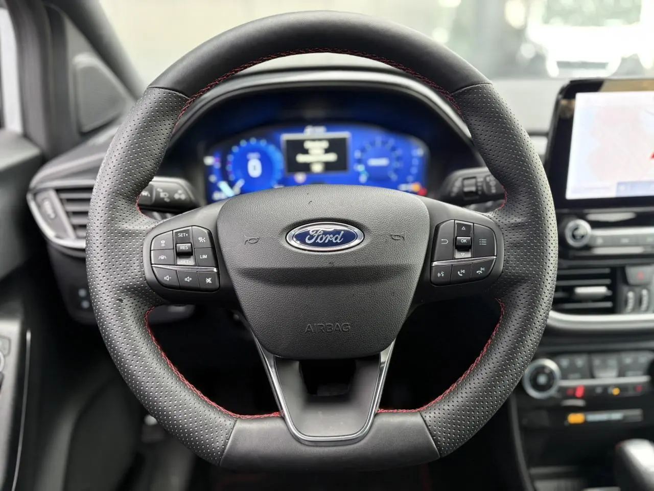 Vue rapprochée du volant ST-Line noir avec surpiqûres rouges du Ford Puma 2023, tableau de bord numérique et écran tactile visibles.