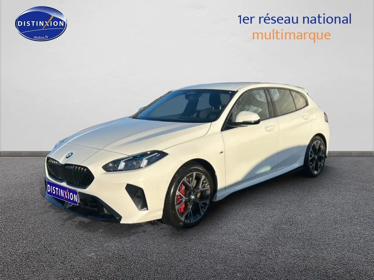 BMW Série 1 blanche alpin vue 3/4 avant droit, jantes 18 pouces bicolores et étriers de frein rouges visibles.