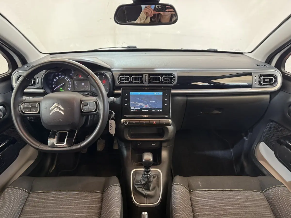 Vue intérieure avant du tableau de bord noir et volant cuir de la Citroën C3 blanche avec écran tactile central et boîte manuelle.