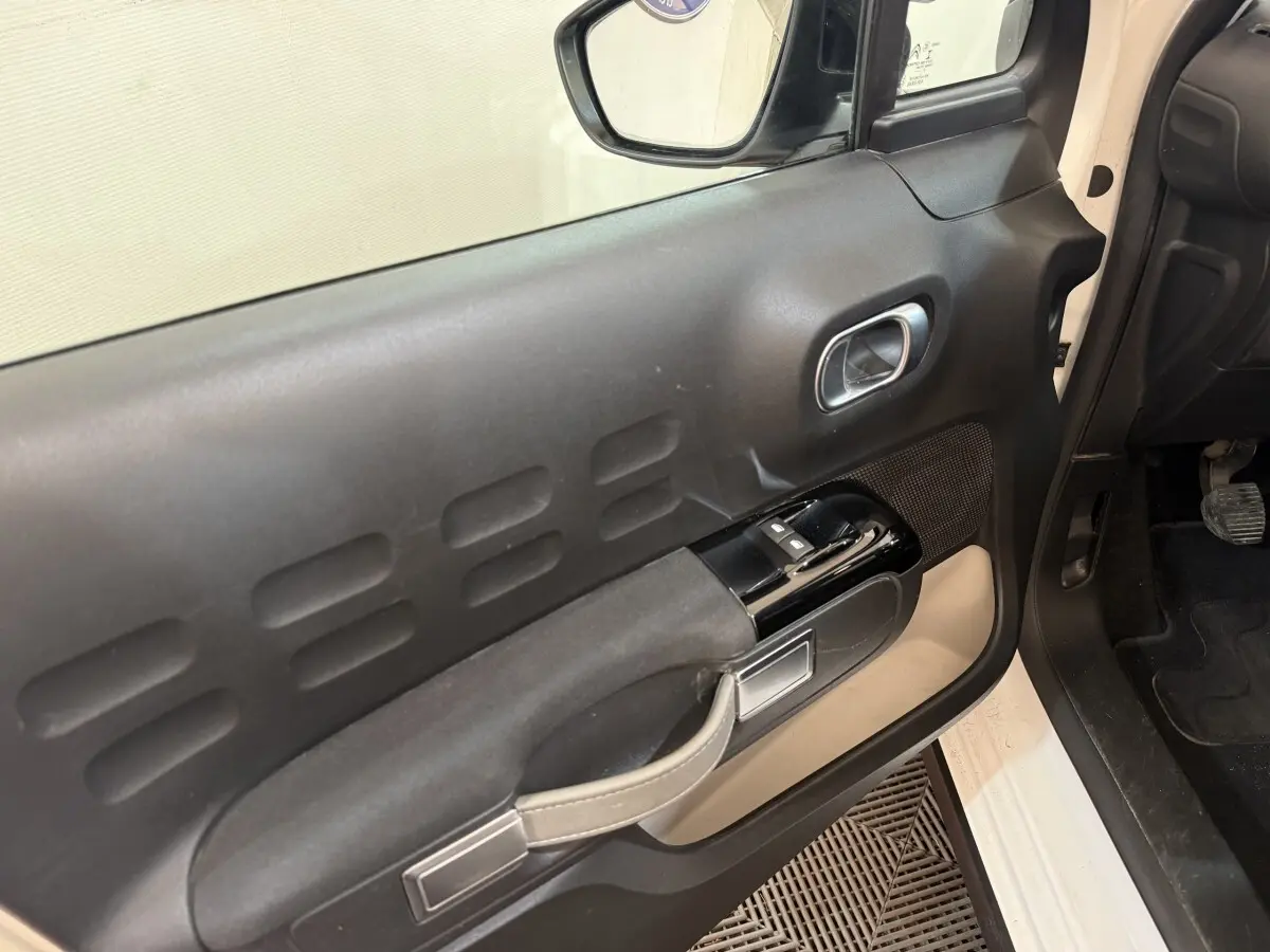 Vue intérieure du panneau de porte côté conducteur d'une Citroën C3 blanche, avec commandes de vitres et poignée intégrée.