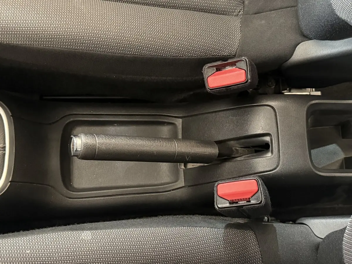 Vue plongeante sur le frein à main noir et les ceintures de sécurité rouges de la Citroën C3 blanche, intérieur tissu gris.