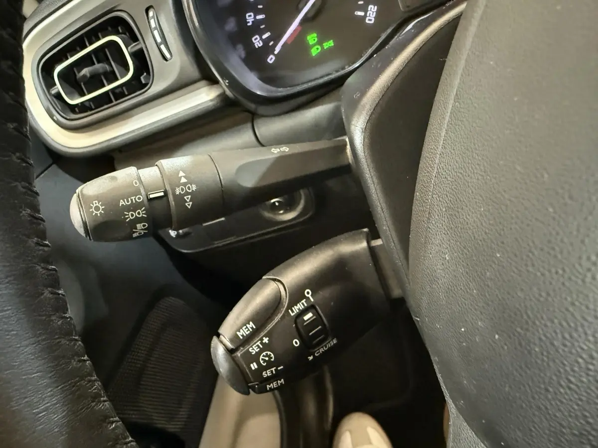 Gros plan sur la commande de régulateur de vitesse et les commandes d’éclairage côté gauche du tableau de bord noir d’une Citroën C3 blanche.