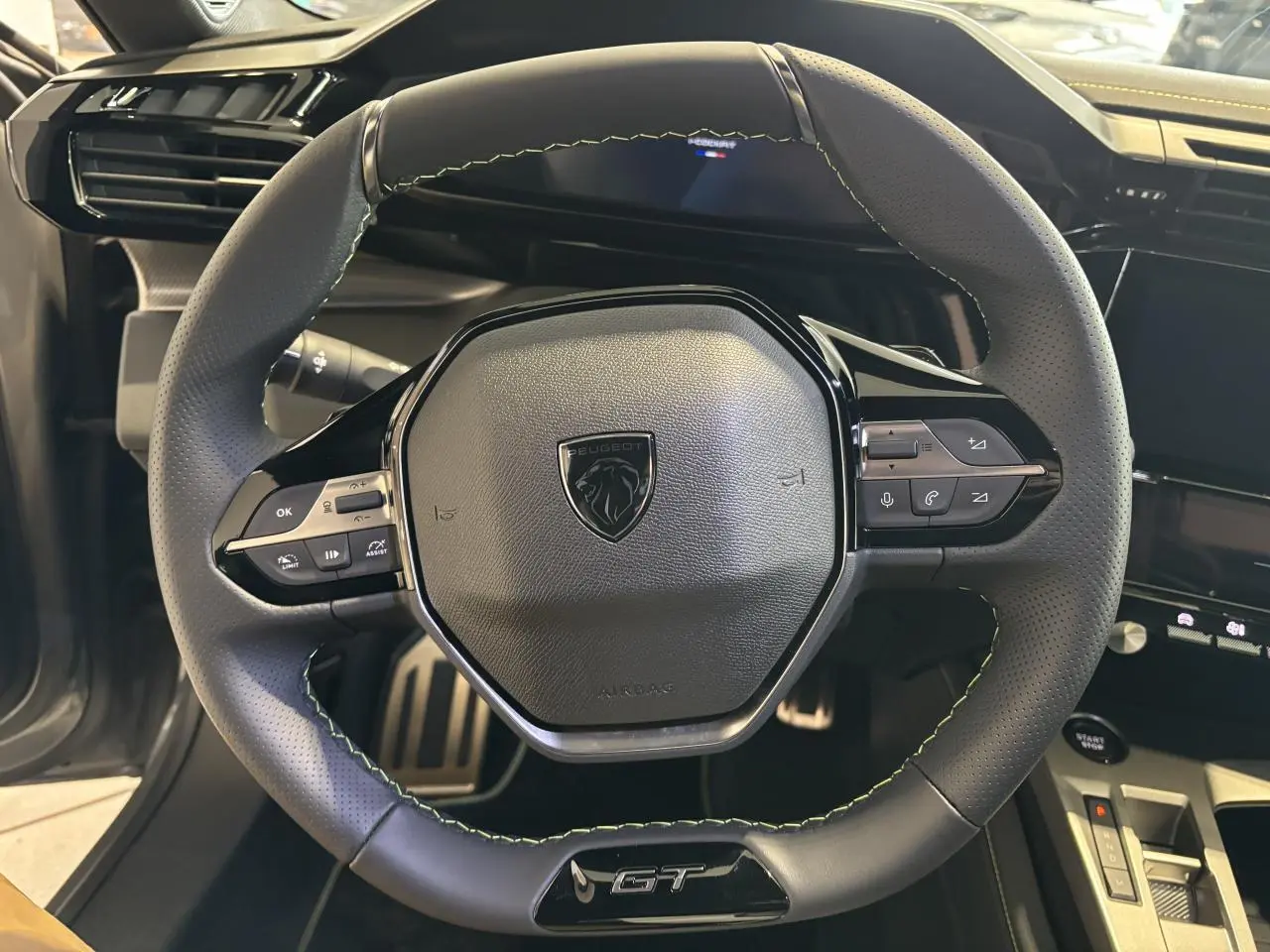 Volant GT en cuir noir avec surpiqûres vert Adamite dans l'habitacle du Peugeot 308 gris Selenium, vue de face rapprochée.