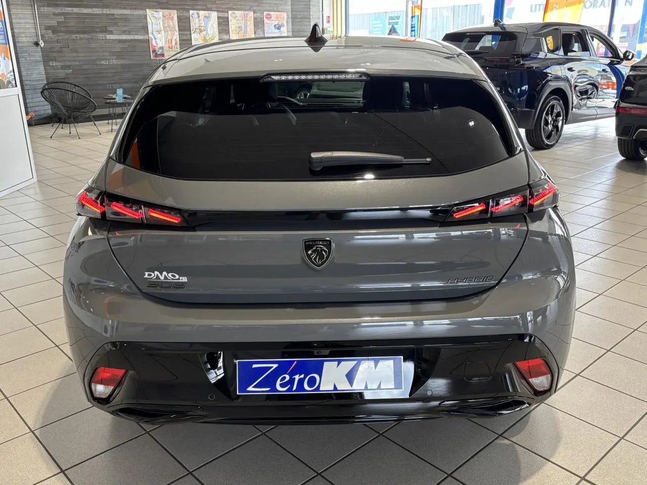 Vue arrière d'une Peugeot 308 hybride gris selenium avec feux arrière LED 3 griffes et bandeau noir brillant en concession.