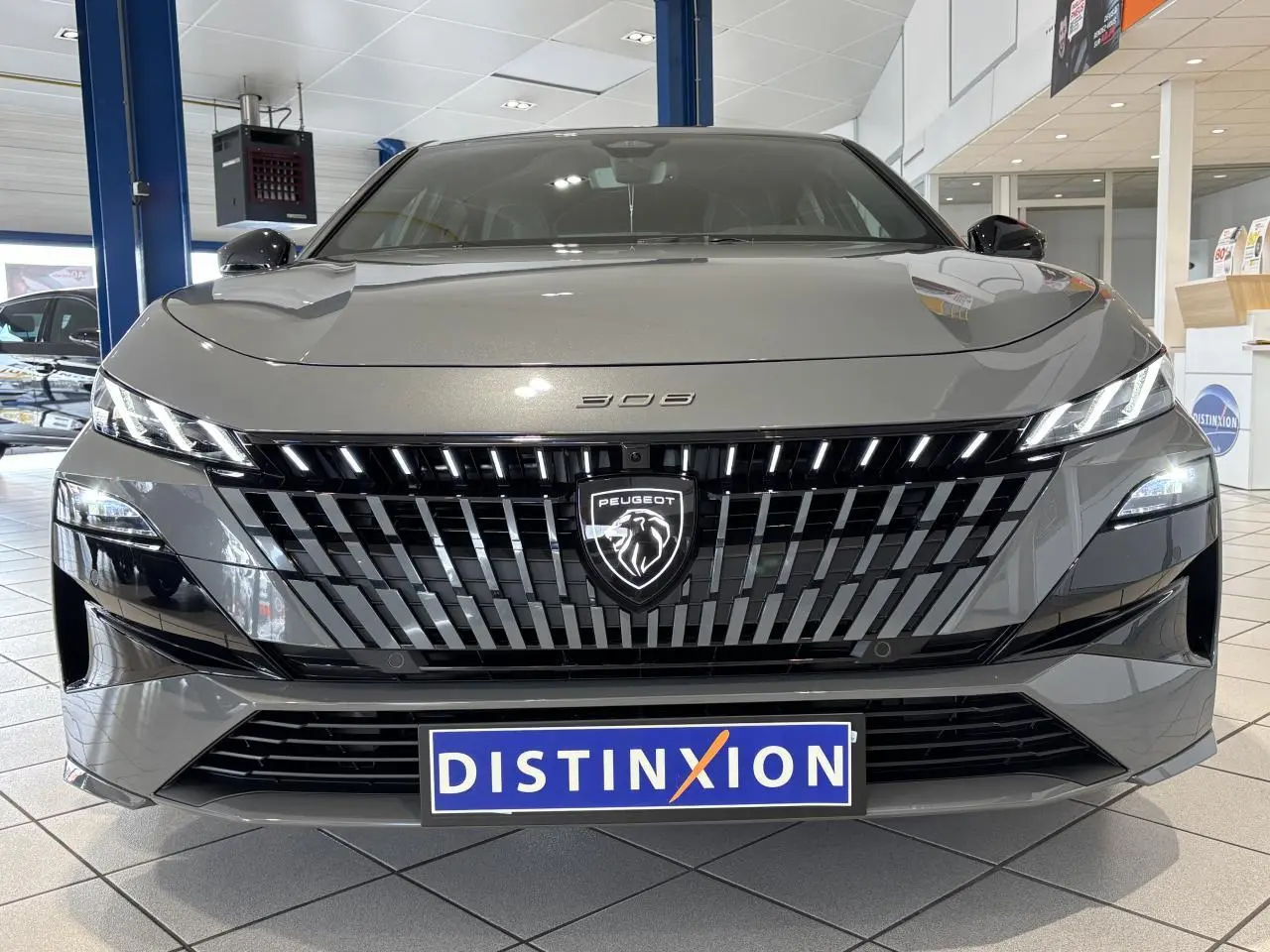 Vue avant d'une Peugeot 308 gris selenium avec calandre noire brillante et logo lion illuminé en concession.
