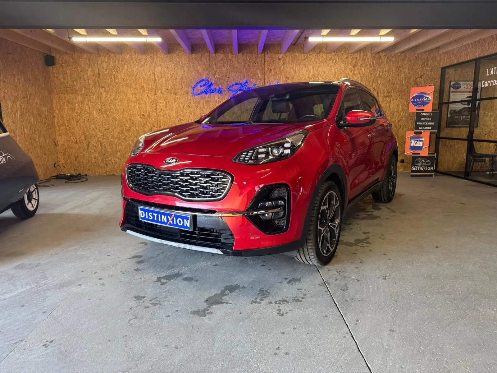 KIA Sportage 1.6 CRDI rouge en 3/4 avant droit, avec calandre noire et jantes alliage visibles en intérieur showroom.