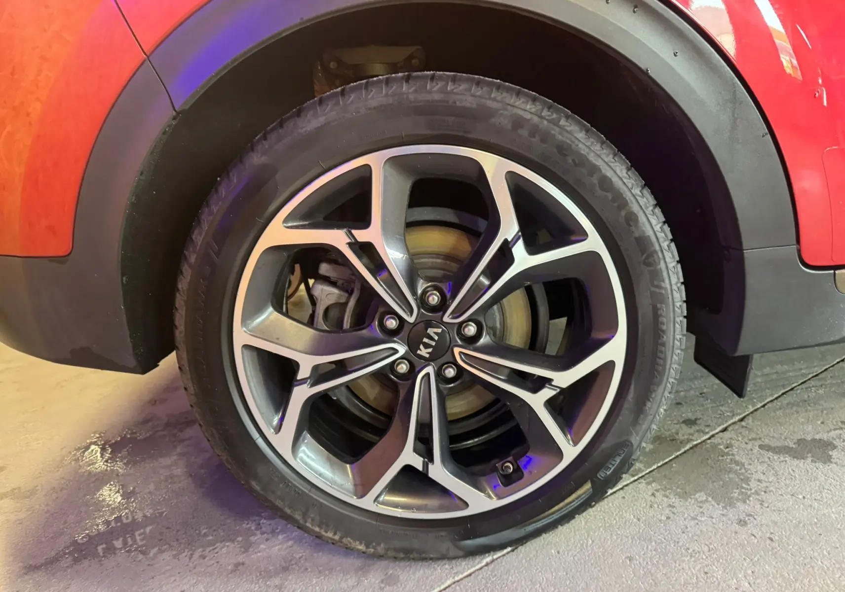 Gros plan sur la roue avant droite du KIA Sportage rouge 2019, mettant en valeur la jante alliage au design moderne.