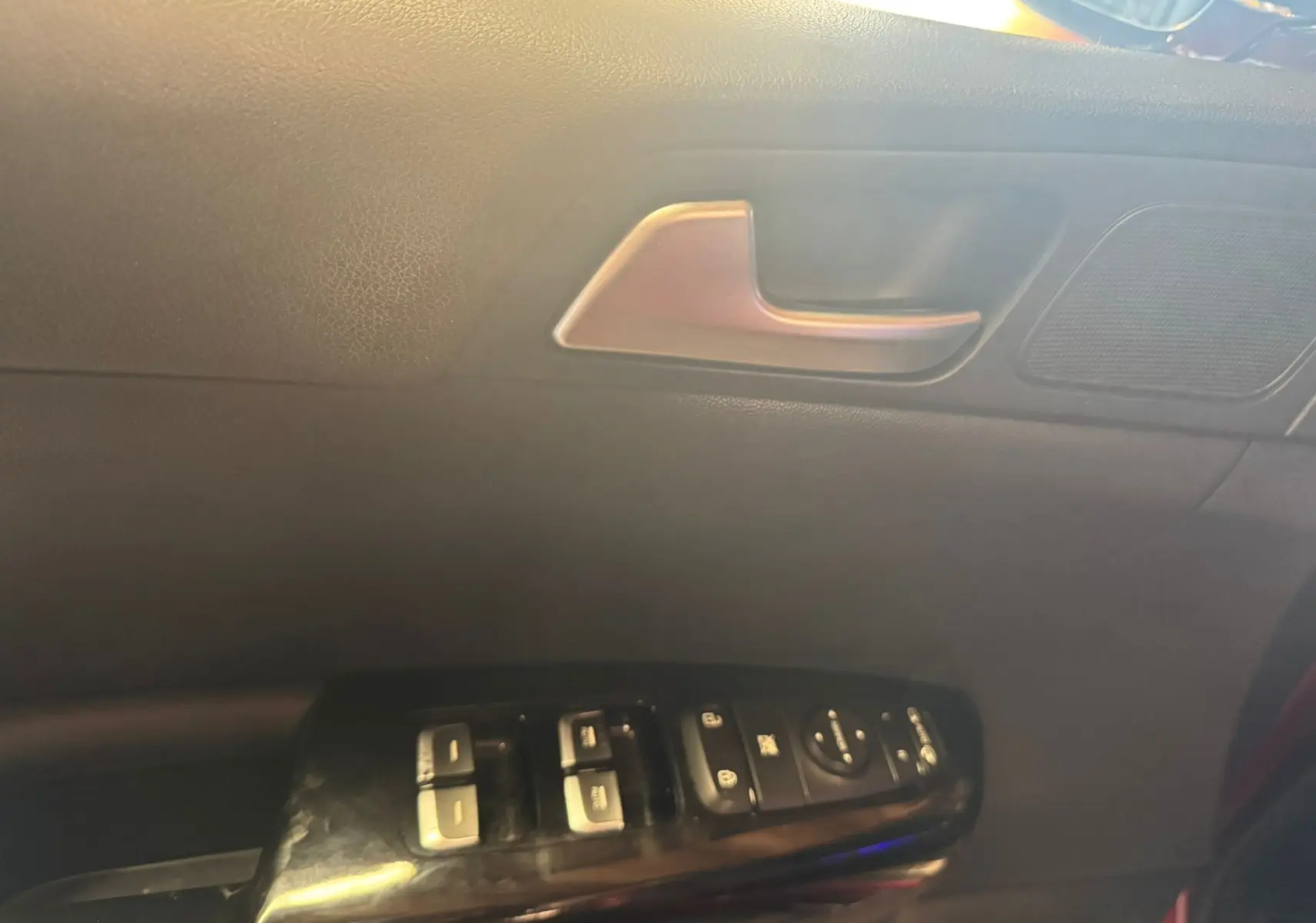 Détail de la porte côté conducteur d’un KIA Sportage rouge 2019, avec commandes des vitres et poignée intérieure argentée.