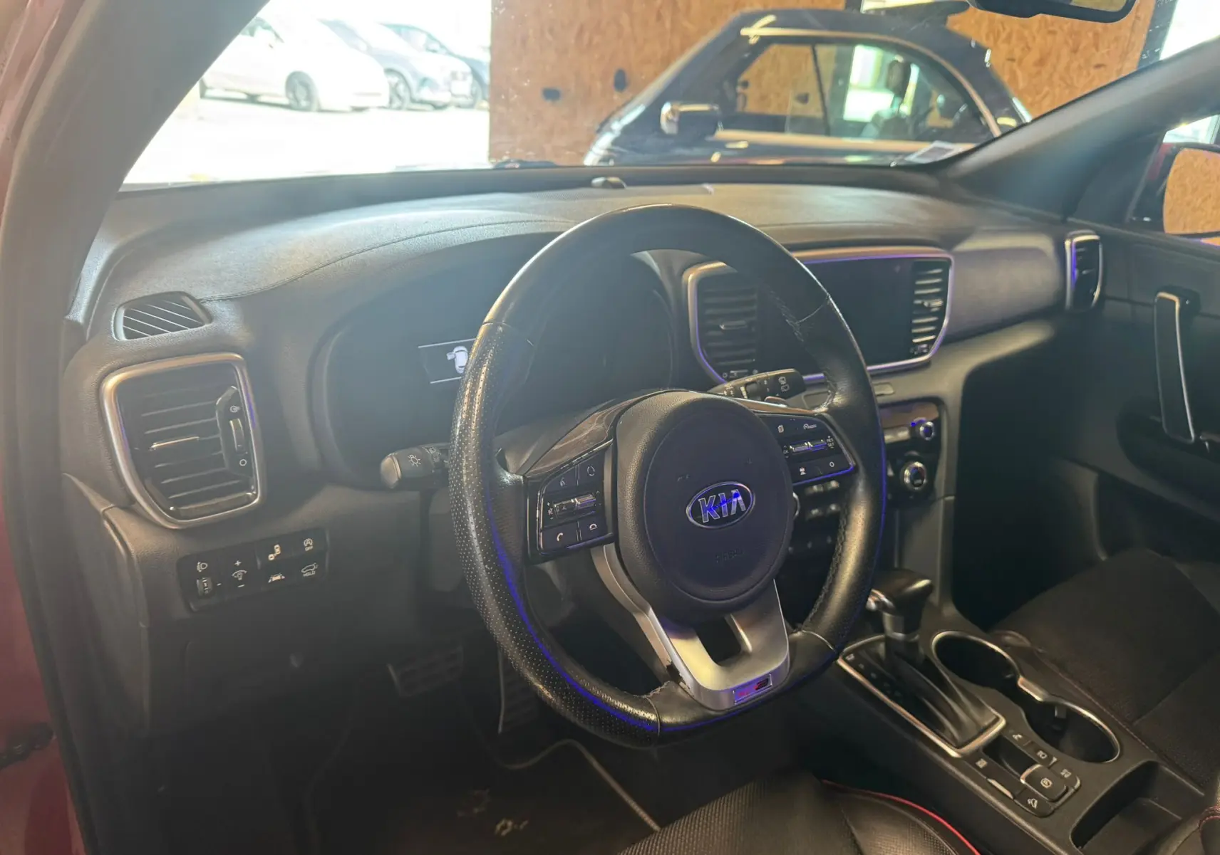 Vue intérieure du poste de conduite du Kia Sportage rouge 2019, avec volant cuir noir et tableau de bord moderne.