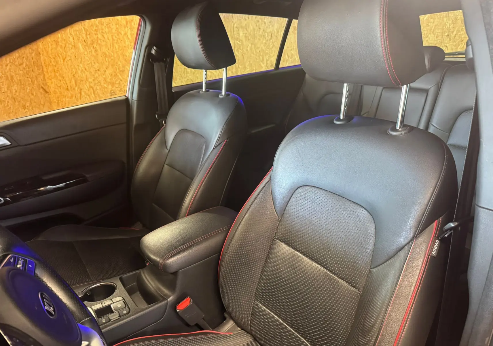 Vue intérieure côté conducteur du Kia Sportage 2019, sièges cuir noir avec surpiqûres rouges et accoudoir central.
